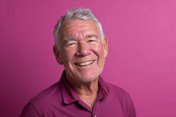 A man in a purple shirt is smiling in front of a pink background