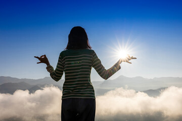 Panorama back view of woman is relaxingly practicing meditation yoga at top of misty mountain with...