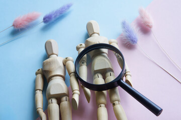Wooden anthropomorphic mannequins of a man and a woman and a magnifying glass on a gendered pink...
