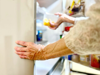 冷蔵庫から食品のケースを取り出す高齢女性の手