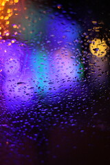 Regentropfen auf Scheibe vor buntem Licht