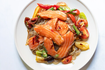 Spicy salad with fresh salmon and potato noodles mixed fermented fish sauce on white plate.