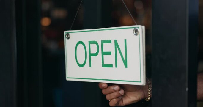 Open, small business and hand of person with sign at storefront window in coffee shop at start of service. Restaurant, store and closeup on change of signage, notice and information on board in diner