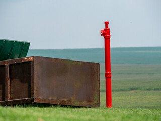 Un poteau rouge à proximité d'une benne à ordure rouillé au milieu d'un paysage verdoyant