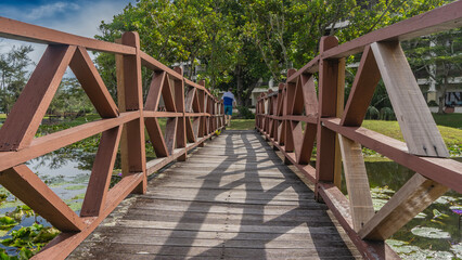 A plank pedestrian bridge with wooden railings spans the river. A man walks away across a green...