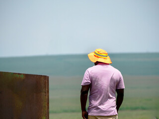 Un travailleur sous le soleil portant un chapeau vu de dos avec un arrière plan de terre agricole
