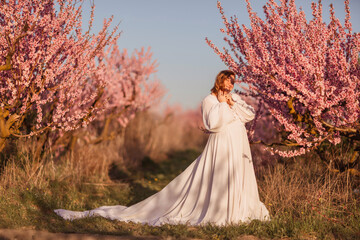 Woman blooming peach orchard. Against the backdrop of a picturesque peach orchard, a woman in a long white dress enjoys a peaceful walk in the park, surrounded by the beauty of nature.