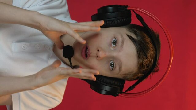 European boy 9 years old streamer in headphones with a headset looks at the camera and blogs live. concept, blogging and streaming on video hosting. vertical video