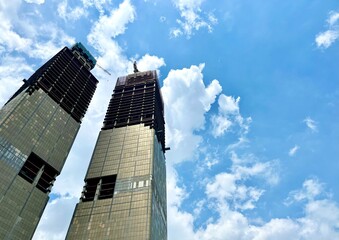 Fototapeta premium Two High and tall under construction huge building tower isolated on horizontal ratio vibrant blue cloudy sky background.