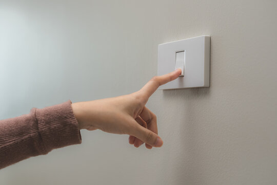 Close up of hand of woman turn off on lighting switch at home room. Finger pushing light switch turn on or off white switch on wall for saving, control power electrical energy, eco environment concept