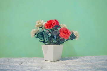 A decorative plastic fake flower bouquet in a white flower vase against a turquoise green wall...
