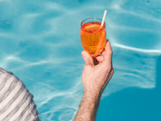 Handsome man with a glass of drink sits near the swimming pool of a cruise liner. Sunny, clear...
