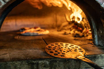 Traditional oven for baking pizza with burning wood and shovel. A stainless steel pizza shovel...