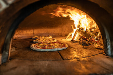 Traditional oven for baking pizza with burning wood and shovel. Several pizzas are baked in a brick...