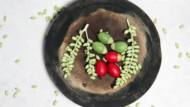 Green and red palm fruits (buah palem) on wooden plate with top view and white background
