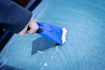 A mans hand holding an ice scraper to clear a car windscreen in winter