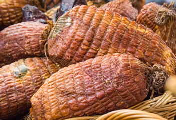 Fresh prepared smoked hams with spices in wicker basket on market stall