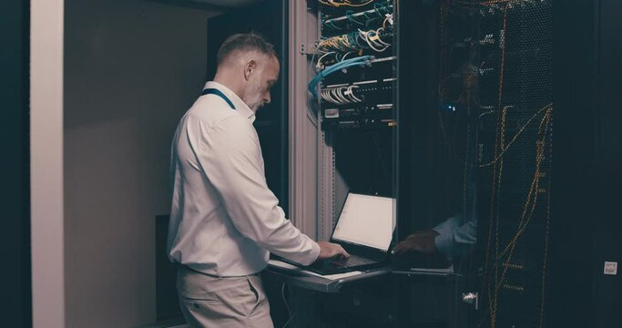 Mature man in data center with laptop, software for network maintenance and engineer in digital storage for web update. Tech screen, system administration and technician in server room with computer