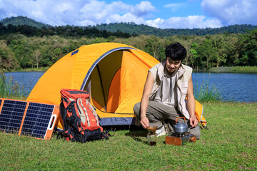 Asian male man making coffee and feeling relax with camping tent beside lake and mountain with mobile solar cell