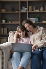 Vertical shot woman and cute little daughter spend weekend watching on-line cartoons, educational videos on laptop, enjoy pastime on internet, make order, purchasing trough electronic commerce website