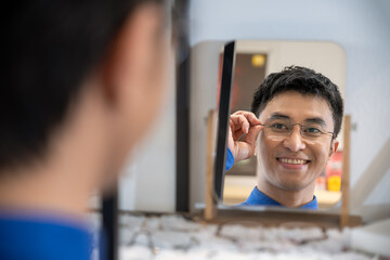 Portrait of Young Asian male man choosing glasses in optical shop, trying eyeglasses. Eyecare concept.