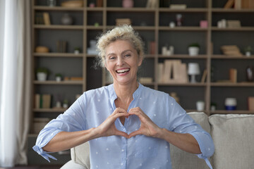 Smiling mature woman looking at camera pose, show symbol of love with joined fingers, demonstrate...