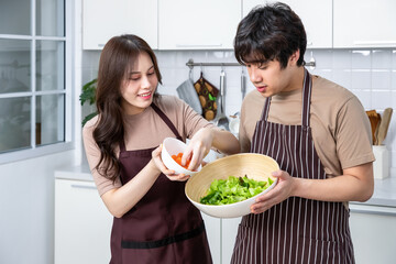 Young Asian couple male man female woman cheerful standing and preparing food for meal, enjoy cooking, in kitchen at home.