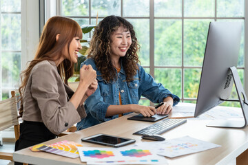 Two smiling and cheerful young Asian female woman businessperson graphic designer working together, meeting and brainstorming, using computer in office.