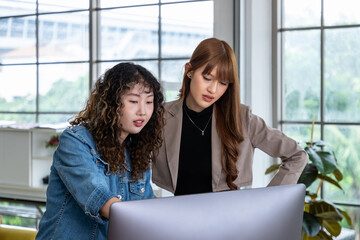 Two young Asian female woman businessperson graphic designer standing and working together, meeting and brainstorming, using computer in office.