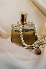 glass perfume bottle with delicate lilac flowers on a textured surface lit by the sun. Top view