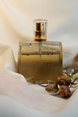 Blank perfume bottle with gold and marble cup in front of a brunch of cherry blossom. Photography in beige tones