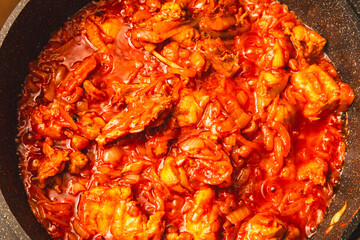 Chicken meat is stewed in tomato in a frying pan