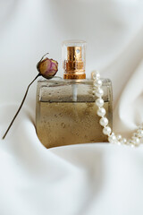 glass perfume bottle with delicate lilac flowers on a textured surface lit by the sun. Top view