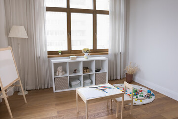 Empty modern playroom with diverse accessories for games, creative hobby, children pastime and elementary development. Interior of cozy nursing with whiteboard, comfortable furniture and toys, nobody