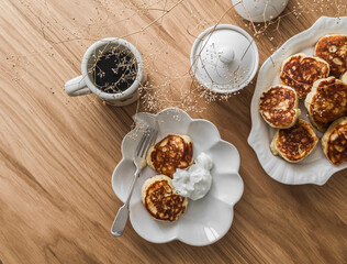 Breakfast served on a wooden table - coffee and pancakes with sour cream, top view