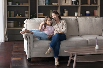 Young caring mother relax with little kid at home, sit on cozy sofa in living room, lead...