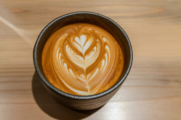Cup of coffee with latte art on wooden table.