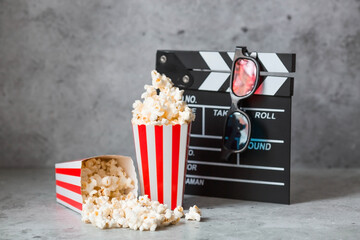 A banner for the film industry. A movie date. A movie camera, 3D glasses, popcorn in striped cups on a stylish concrete gray background. The premiere of the film.
