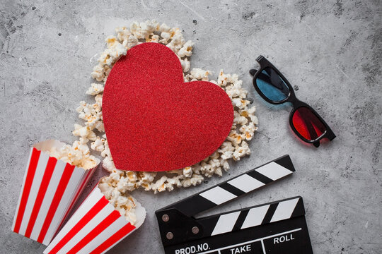 A banner for the film industry. A romantic movie date. A movie camera, 3D glasses, popcorn and a popcorn heart on a stylish concrete-gray background. The film will premiere on Valentine's Day.