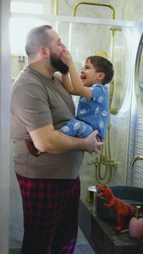 Vertical shot of father and little son in pajamas cuddling and having fun in the bathroom in the morning
