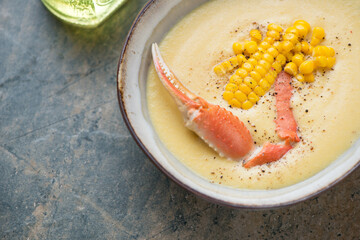 Bowl of corn chowder with crab on a grey and beige granite background, horizontal shot, middle close-up, selective focus