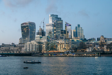 London City skyline at dusk with the River Thames in the foreground.  Illuminated buildings. 