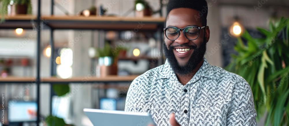 Poster Happy bearded black businessman using digital tablet and mobile app to manage business remotely at office.