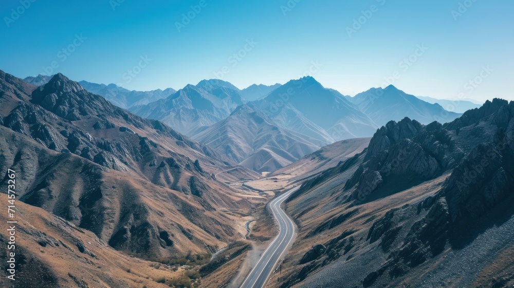 Poster an aerial view of a mountain range with a road winding through the center of the mountain range in t