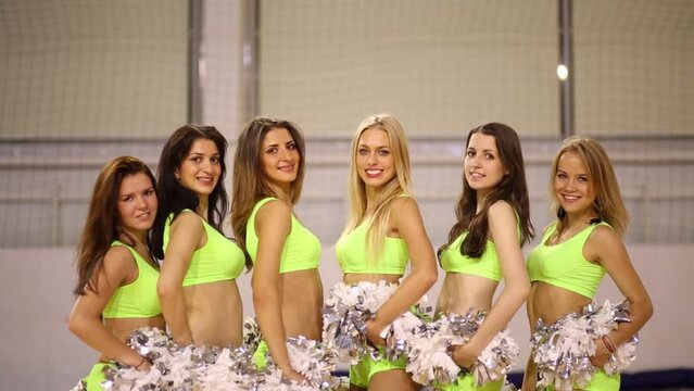 Six smiling women pose with shiny pompons in gym hall
