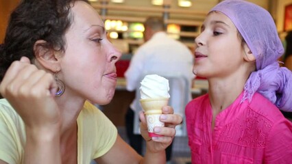 Happy mother and daughter lick sweet ice cream in cafe