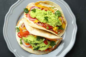 Delicious tacos with guacamole, meat and vegetables on black table, top view