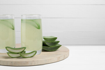 Tasty aloe juice in glasses and cut fresh leaves on white table, space for text