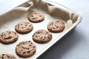 Baking pan with chocolate chip cookies on gray table, closeup
