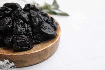 Sweet dried prunes on white tiled table, closeup. Space for text